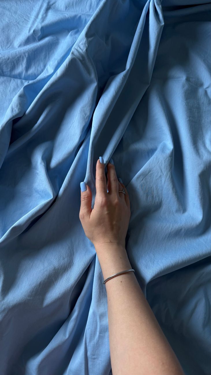 A woman's hand gracefully touches soft blue fabric, creating elegant folds and drapes.