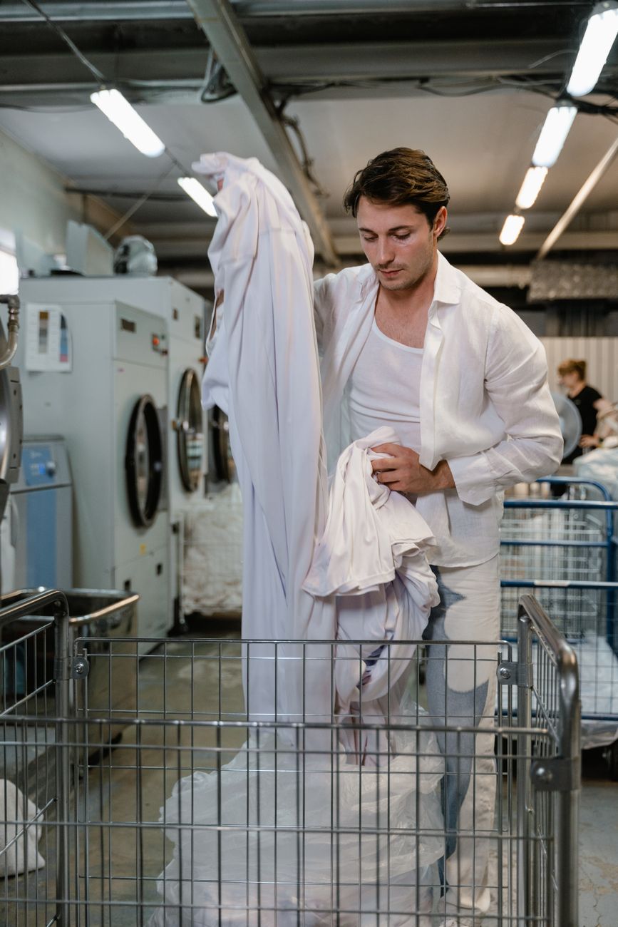 Adult man organizing white linen in a commercial laundry facility.