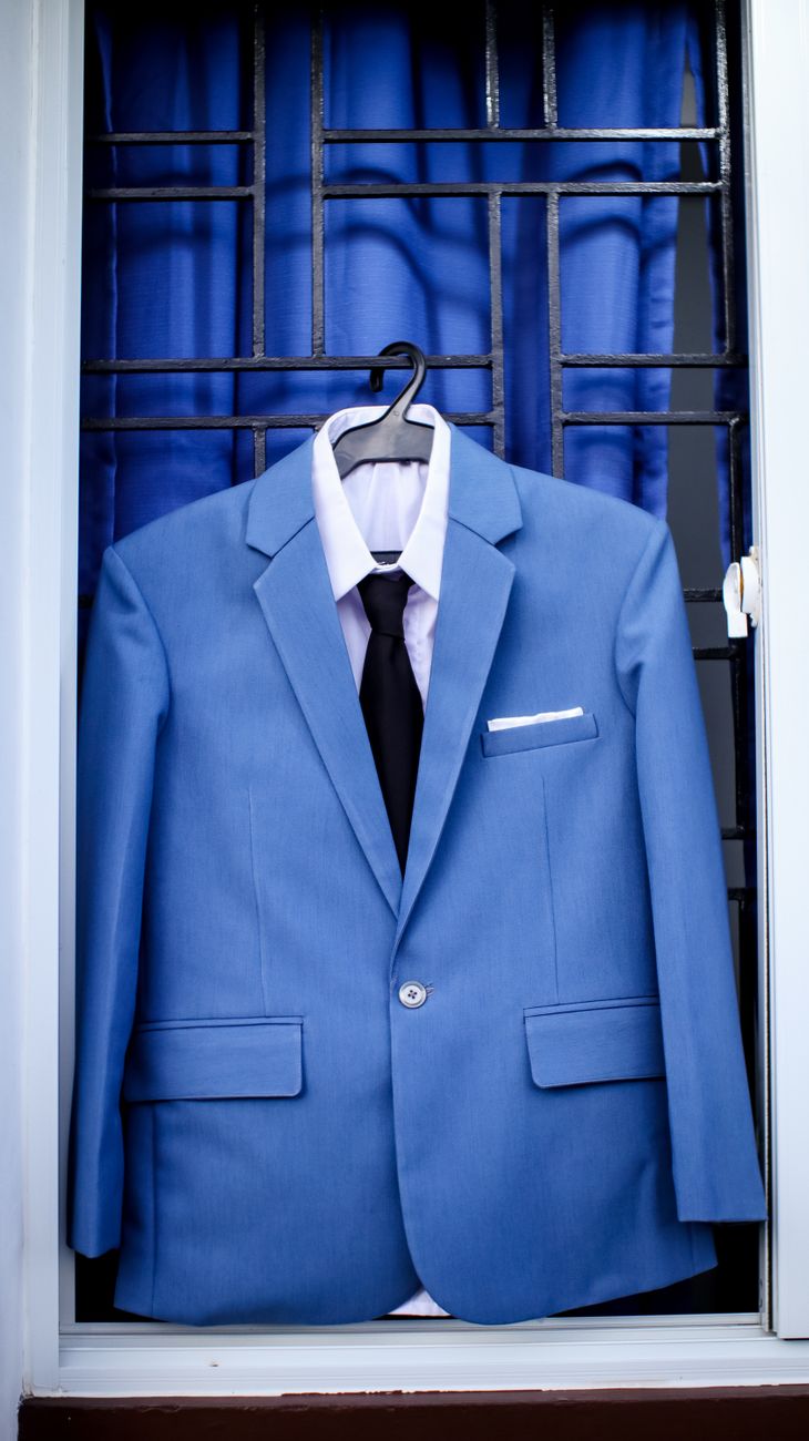Classy light blue suit on hanger with black tie and white shirt placed on window bars