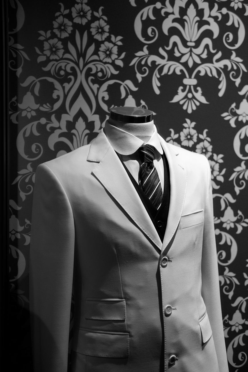 Sophisticated white dinner jacket displayed on mannequin against classic damask wallpaper.